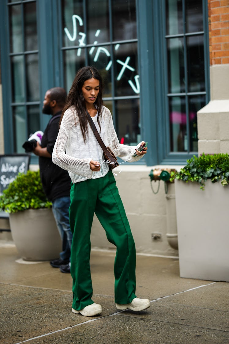 A guest wearing a dark brown leather bag, a white ripped long sleeves t-shirt, dark green flared pan...