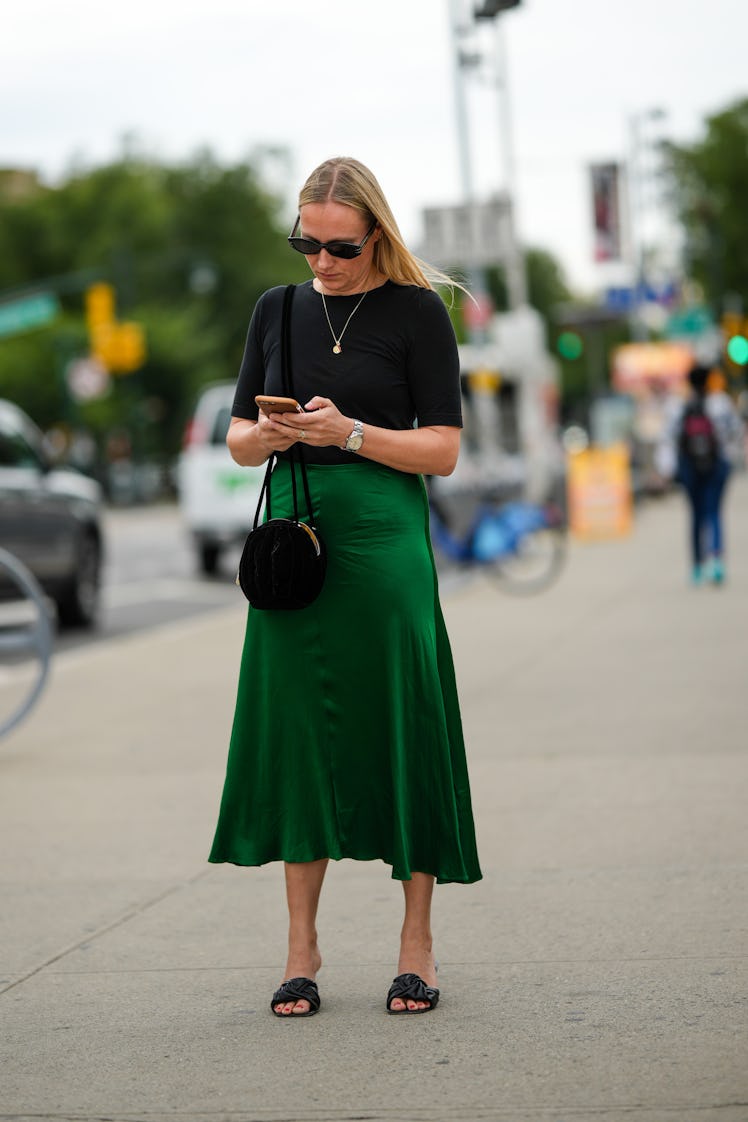 A guest wearing black sunglasses, a black short sleeves t-shirt and a dark green silk skirt with a b...