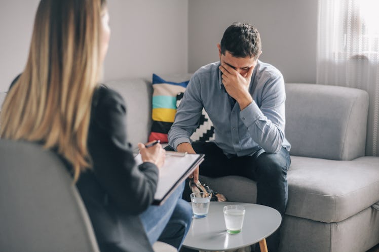 A man holds his head in his hands while speaking to a female therapist.