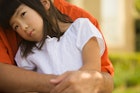 一个孩子坐在她爸爸的腿上，得到一个拥抱，把头靠在他的胸前。