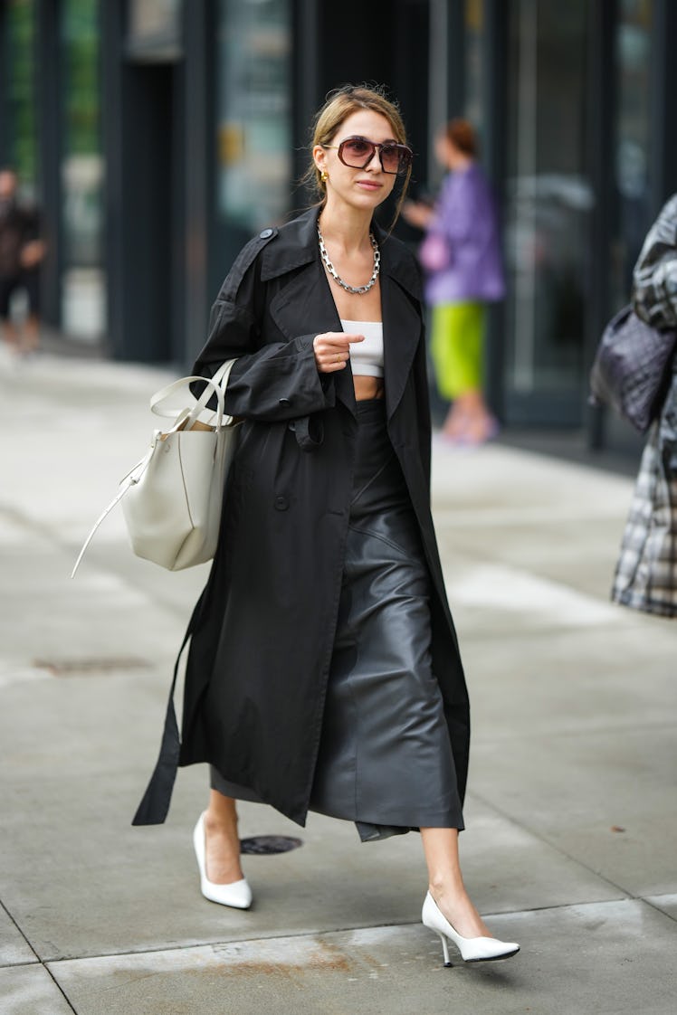 A guest wearing a white shoulder-off cropped top, a black trench coat, a black leather midi skirt, a...