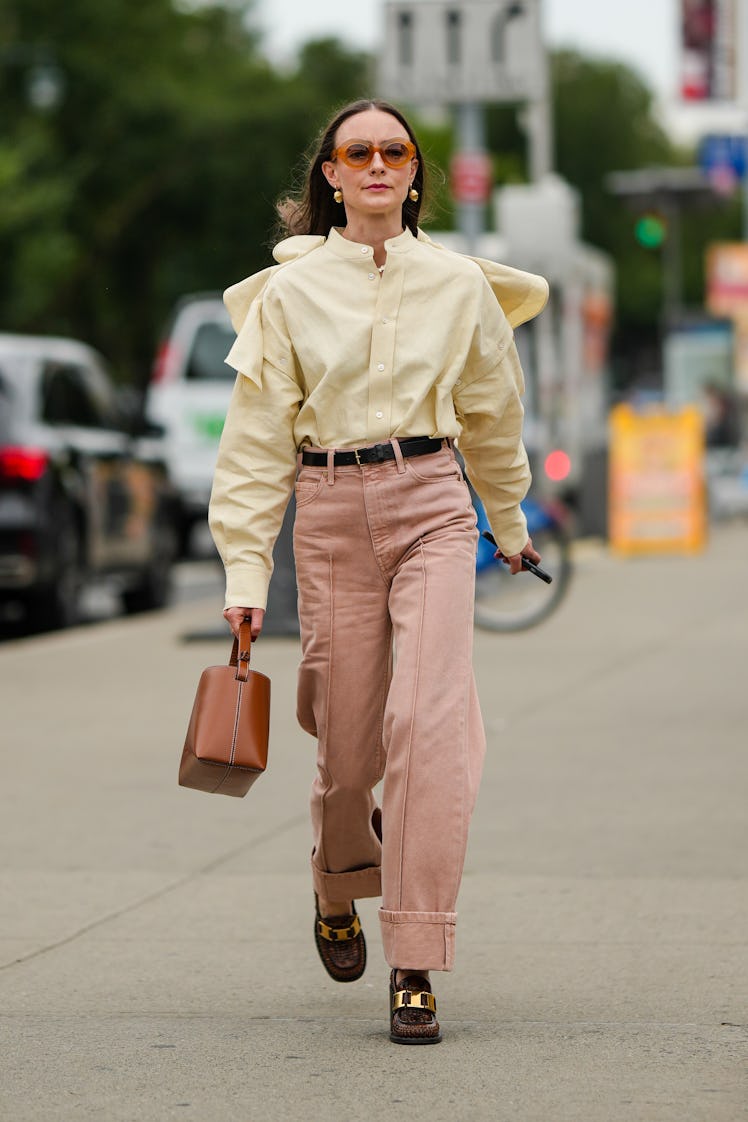 A guest wearing orange sunglasses, gold earrings, a pale yellow linen shoulder shirt and pale pink d...