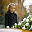 A girl dressed in black stares sadly at a coffin.