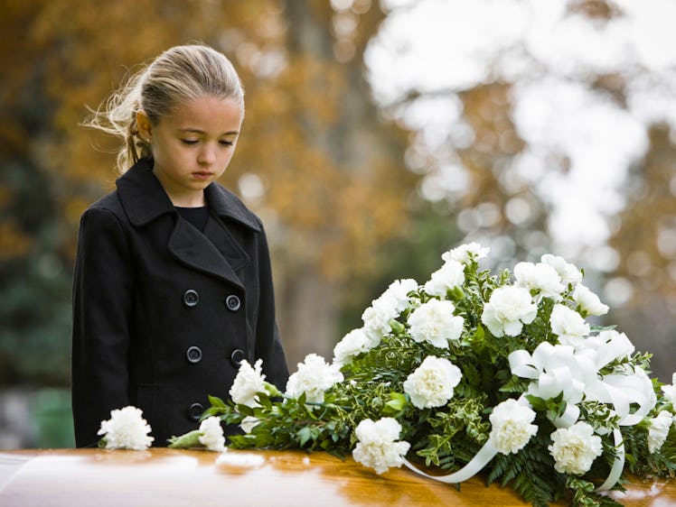 A girl dressed in black stares sadly at a coffin.