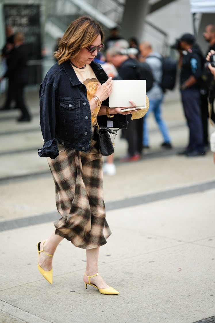 A guest wears a black denim jacket, a beige and brown print pattern t-shirt, a brown and beige check...