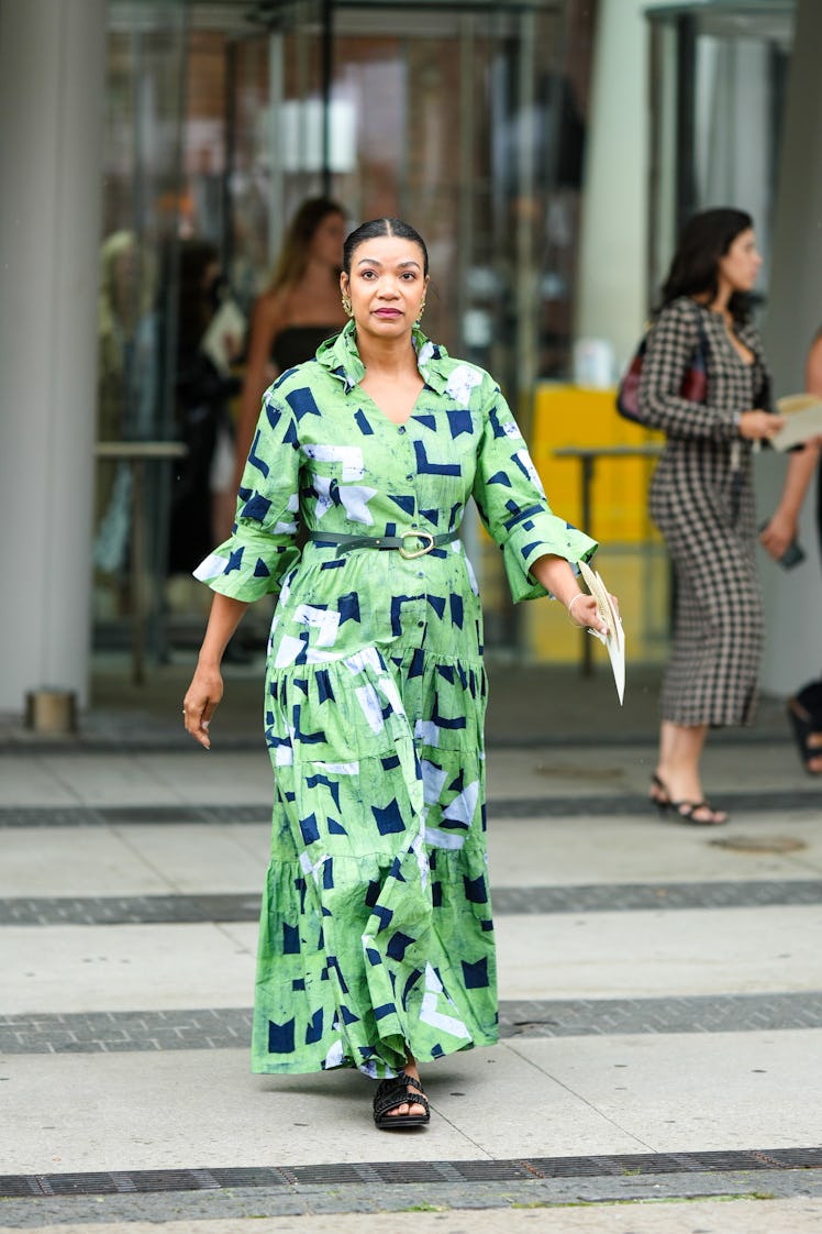 A guest wearing gold earrings, a green with blue and white print long dress with a khaki shiny leath...