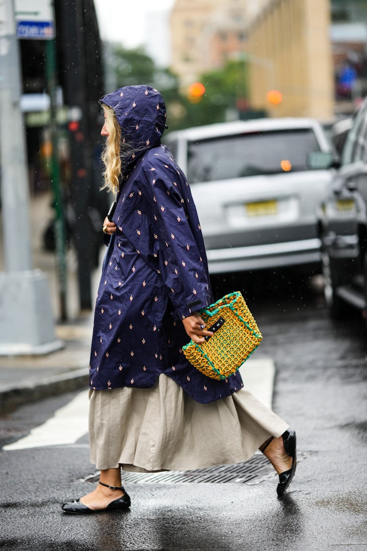 A guest wearing a navy blue oversized coat with a hoodie, a beige long dress and a yellow and green ...