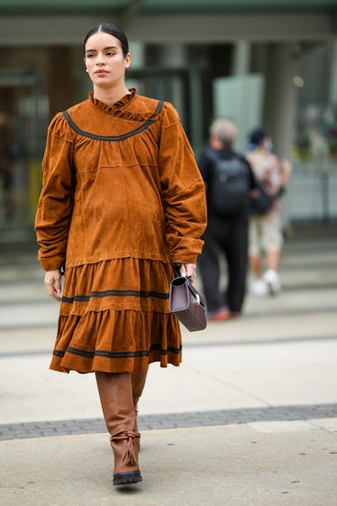 A guest wears a brown suede long sleeves / ruffled / oversized knees dress, a dark brown shiny leath...