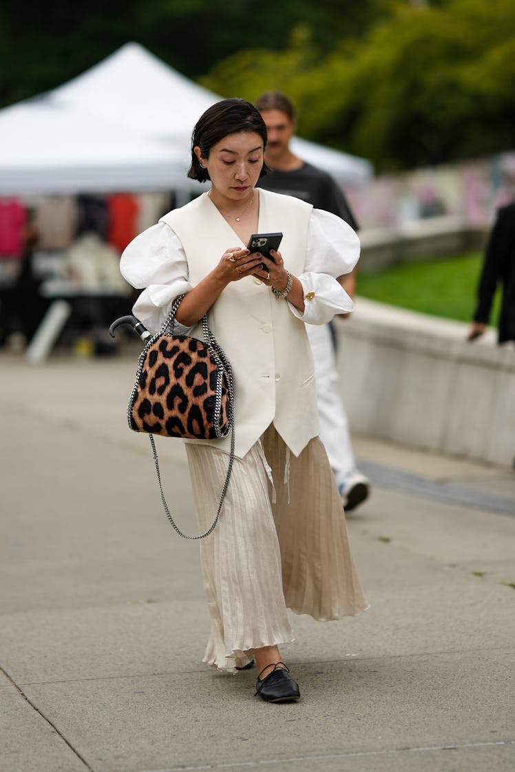 A guest wearing a gold VCA necklace, a white oversized blazer gilet, a beige long skirt and a brown ...