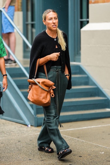 A guest wears a black wool / buttoned cardigan, a black shoulder-off top, a camel shiny leather larg...