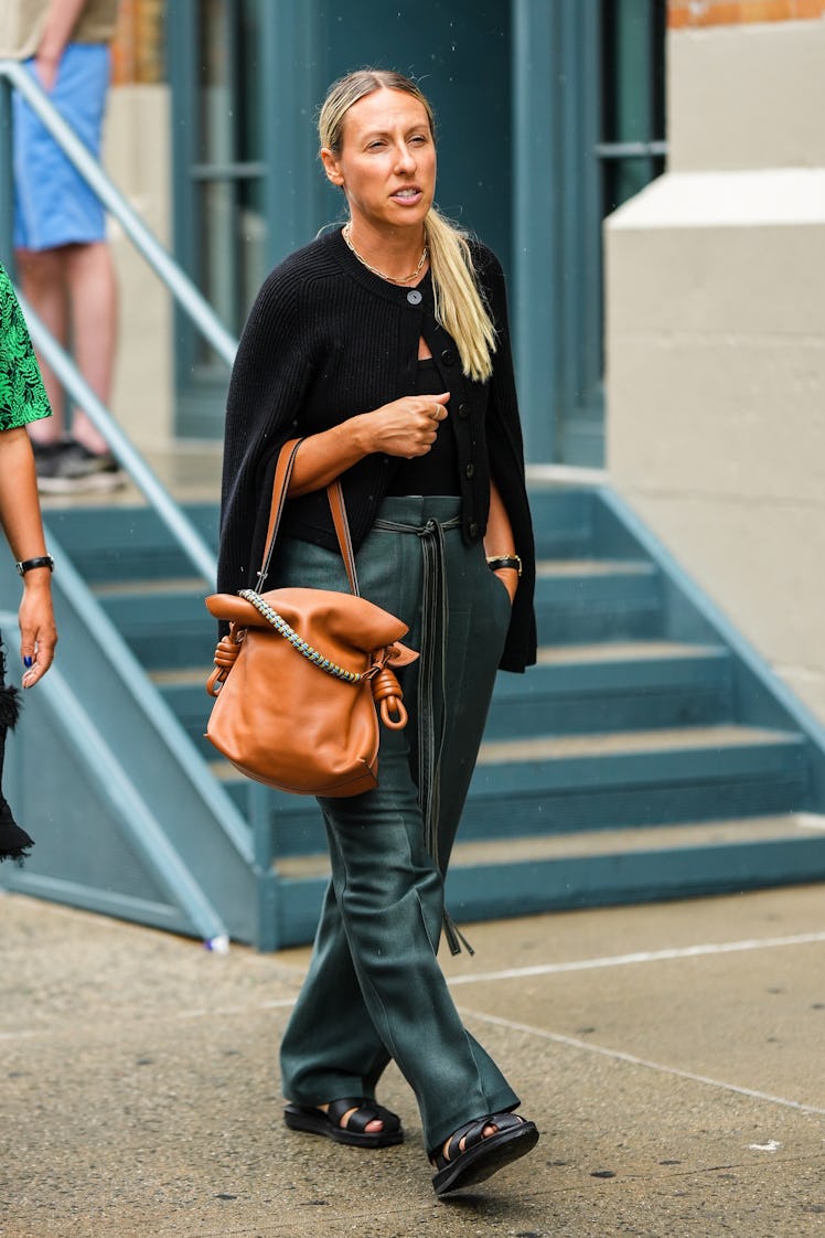 A guest wearing a black wool buttoned cardigan, a black shoulder-off top, a large camel bag and larg...