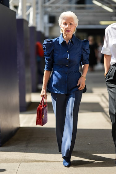 Carolina Herrera wears gold earrings, a navy blue denim puffy shoulder / buttoned blouse, navy blue ...