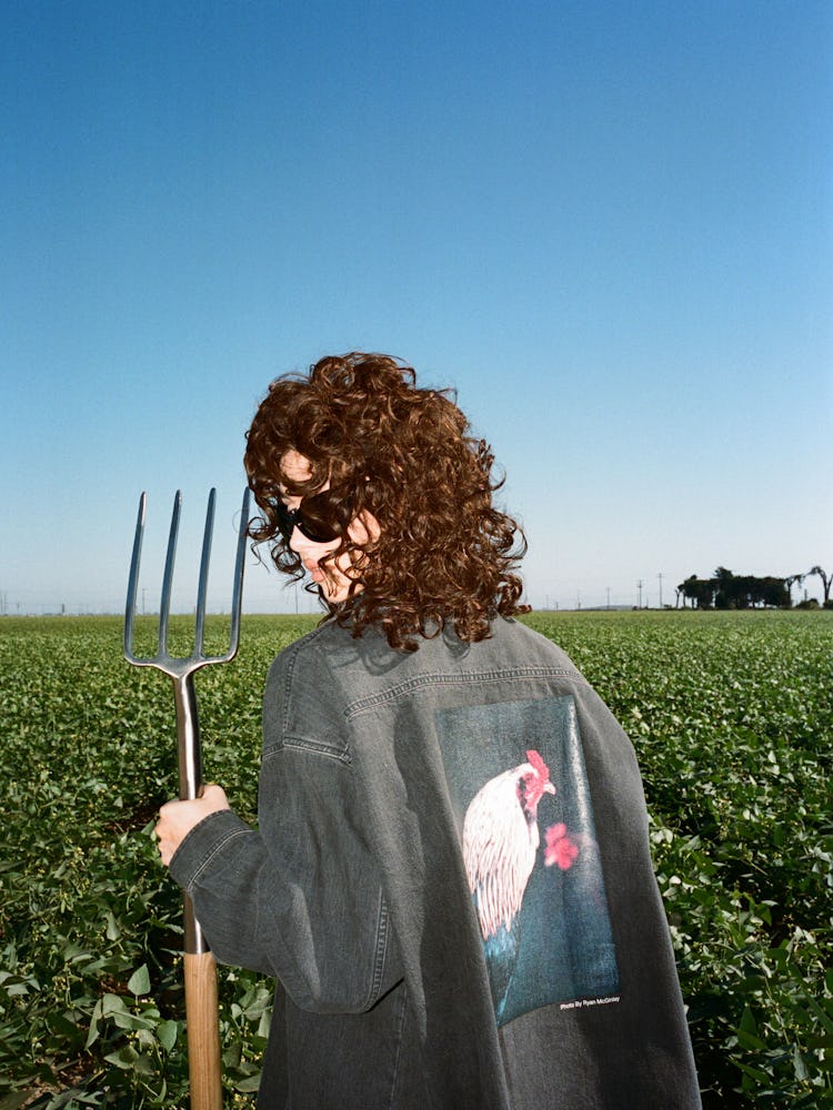 Nadia Lee Cohen wearing a Balenciaga x Sky High Farm shirt in a field holding a pitchfork