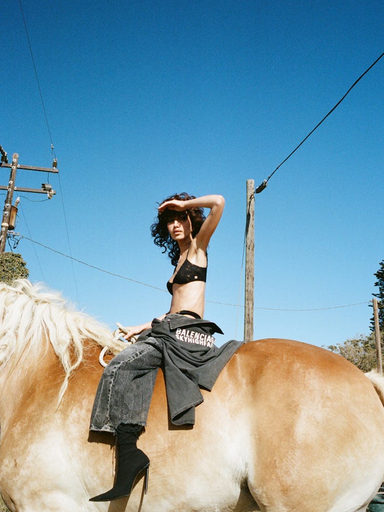 Nadia Lee Cohen sitting on a horse wearing a Balenciaga x Sky High Farm jacket