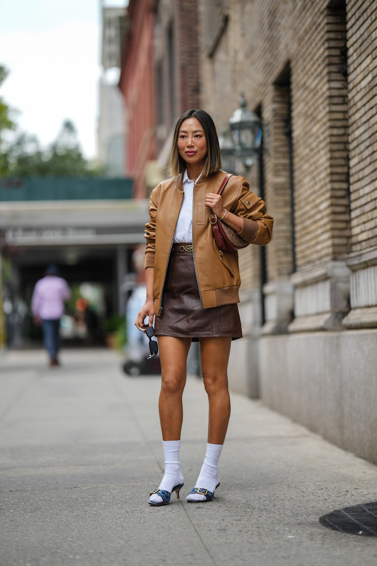 Aimee Song wearing a white shirt, a brown shiny leather bomber coat and a dark brown shiny leather s...