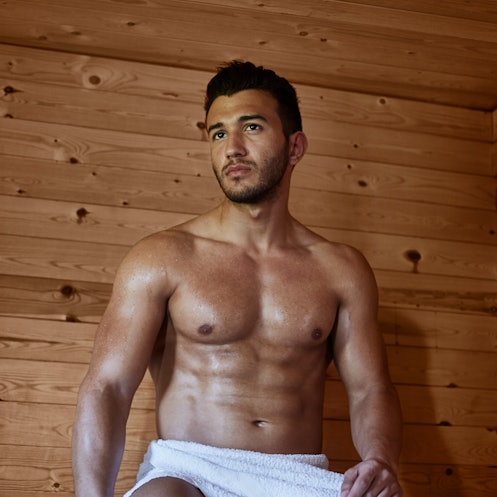 A shirtless man with a towel around his lower half sits in a Finnish sauna.