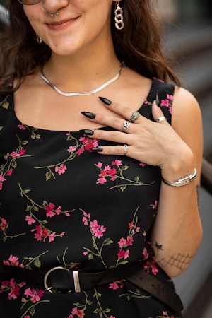 A woman wearing a floral dress over pink pants, a black bag and black platform shoes with black nail...