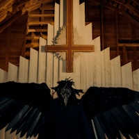 A winged figure in front of an upside-down Christian cross.