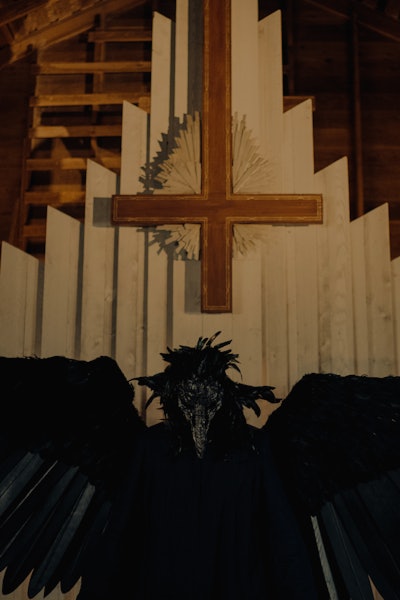 A winged figure in front of an upside-down Christian cross.