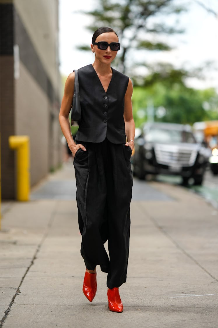 Mary Leest wearing black square sunglasses, sleeveless buttoned gilet, leather bag and pants and red...