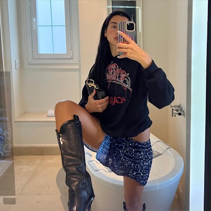 Dua Lipa perching her foot on a vanity while taking a selfie in a mirror