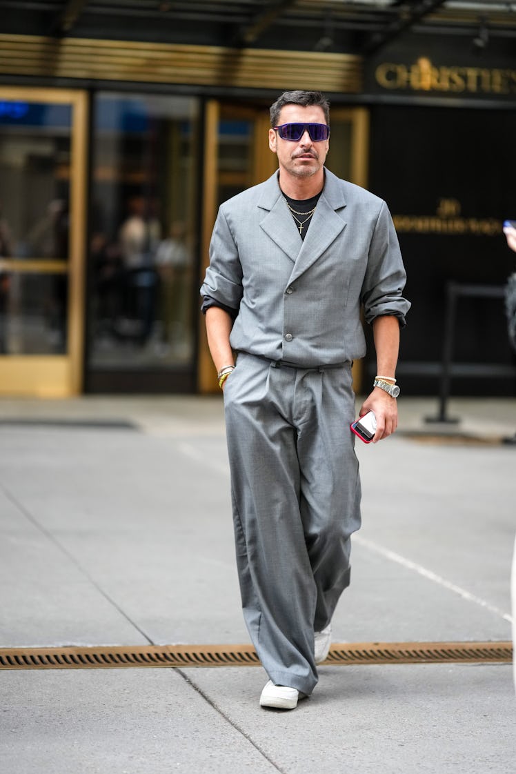 Alex Badia wearing black sunglasses, a black t-shirt, a pale gray blazer jacket and matching pants w...