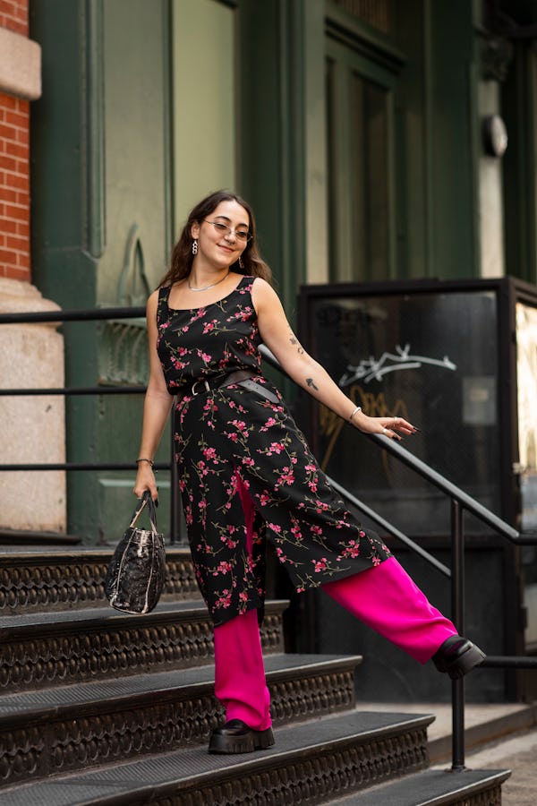 A woman wearing a floral dress over pink pants, a black bag and black platform shoes with one leg li...