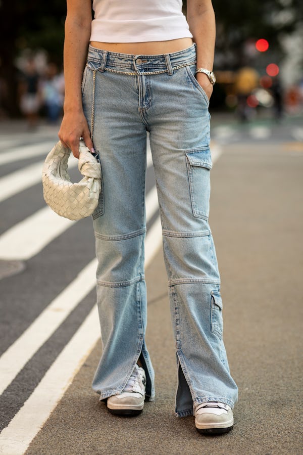 A brunette woman in a white tank top, black sunglasses and low-rise blue denim jeans close-up