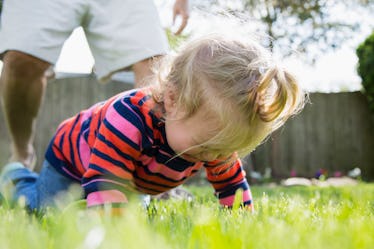 A baby in the grass crying while a parent stands behind.