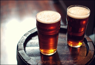 Two glasses of dark beer sitting on a wooden barrel