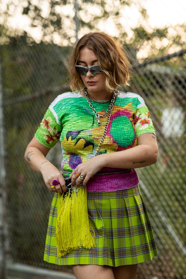 A woman in a floral multi-colored top, green plaid skirt, beige shoes and dad sunglasses close-up