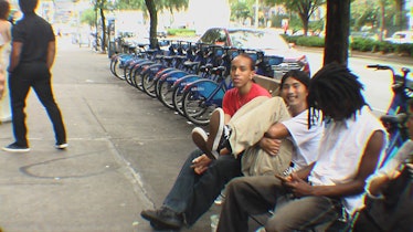 Three people sitting on a bench next to CitiBike dock