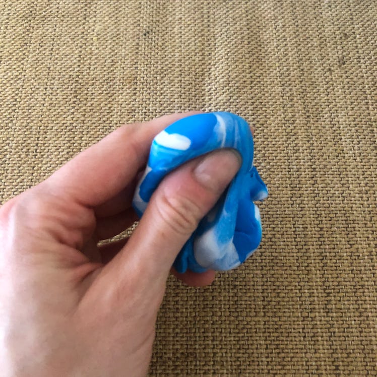 A hand squishing a blob of two different colors of paste between thumb and fingers