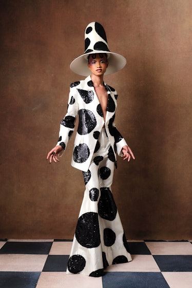 Model walking in a white with black dots Harris Reed hat, blazer, and pants combination