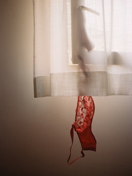 A lacy red bra hanging from a window