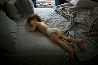 A toddler in a diaper sleeping in a disheveled bed.