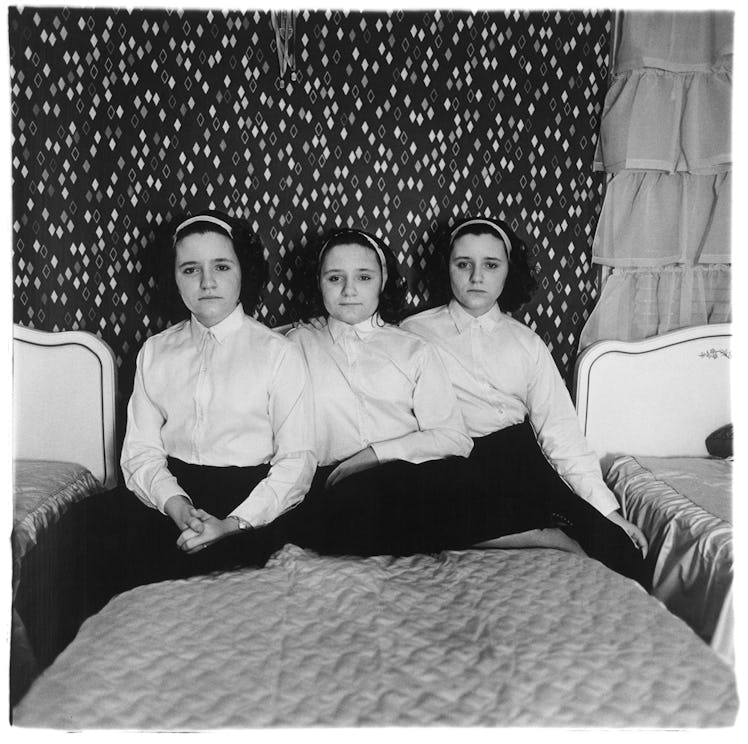 Triplets sitting on a bed in a black-and-white photo taken by Diane Arbus