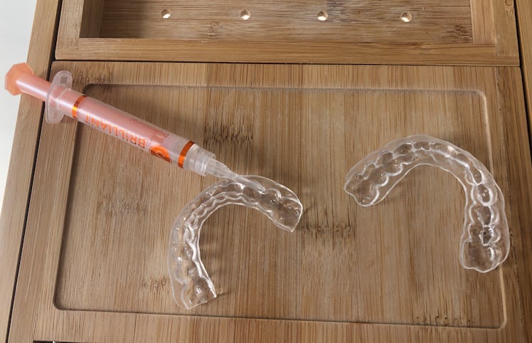 A syringe with clear gel and two clear custom teeth trays.