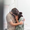 A man comforts his wife after a miscarriage by hugging her while she cries.