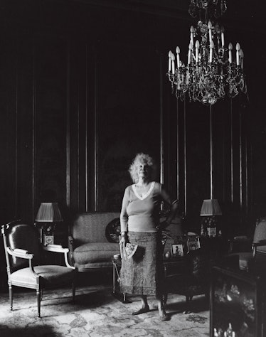 Duchess of Alba at home in her living room standing next to a couch underneath a chandelier 