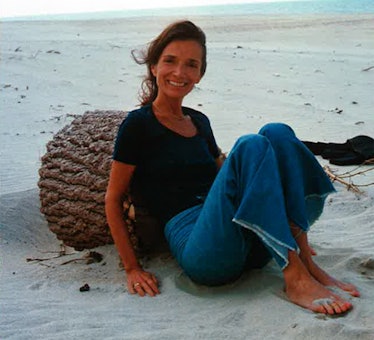 Lee Radziwill sitting on a beach in a black T-shirt and blue denim jeans