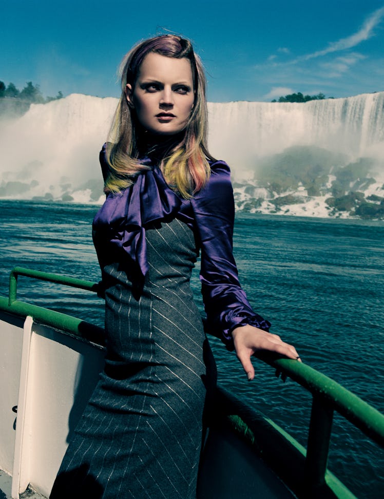 Guinevere van Seenus in a purple satin blouse and a grey pinstripe dress on a boat