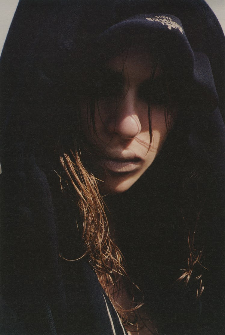 A model posing with a hoodie on her head and shadows only making the lower part of her face visible