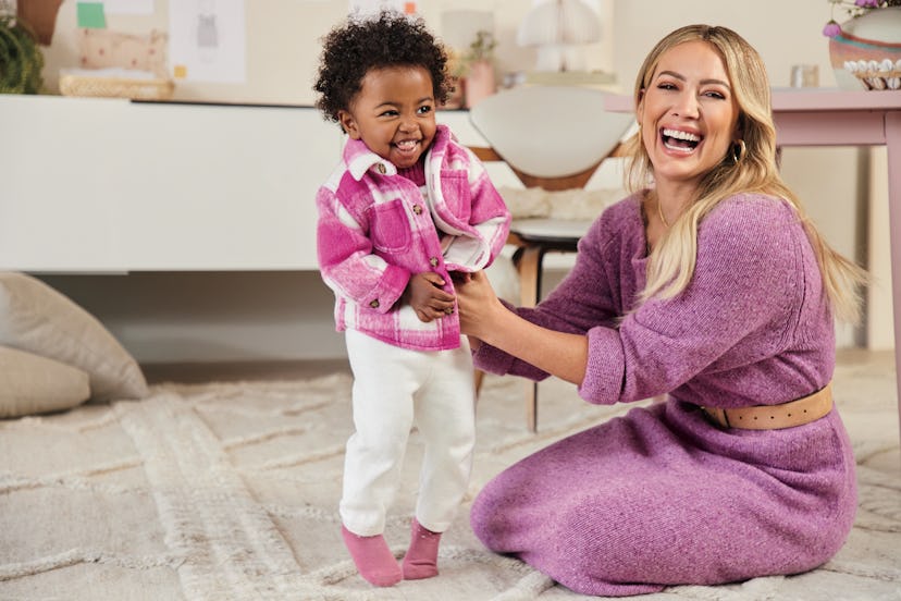 Hilary Duff smiling at the camera and reaching for a cute toddler wearing an outfit from the Hilary ...