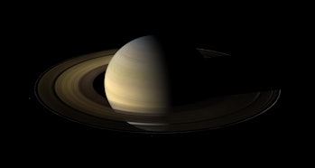 Saturn is shrouded in partial darkness.  Half of the planet is visible and the rings are faint.
