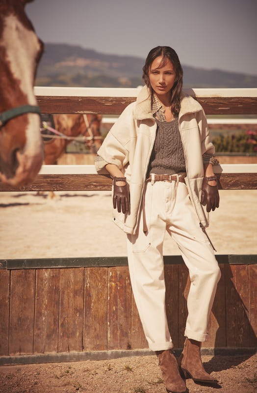 A model in white pants and a matching coat with a grey sweater from the Brunello Cucinelli capsule f...