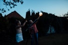 老女人举着灯笼，年轻女孩在望远镜前，两人都望着天空。