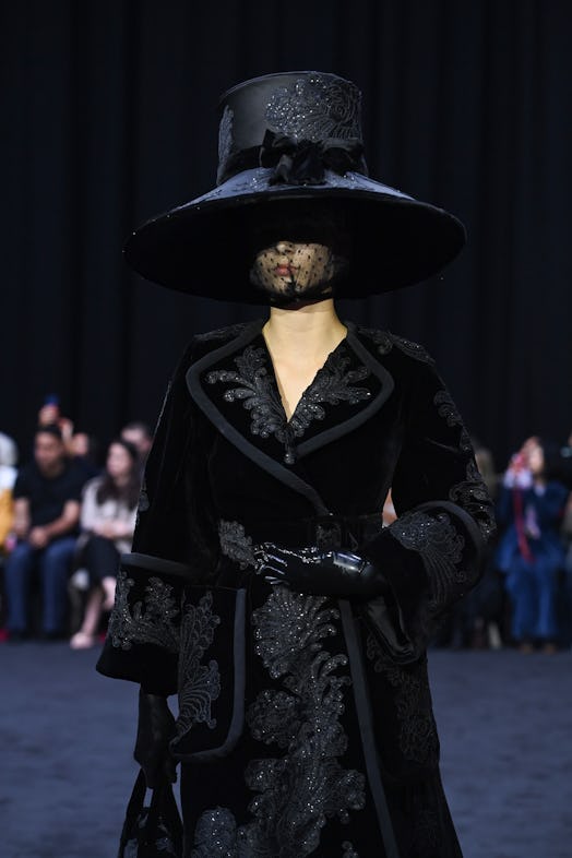 Richard Quinn’s black floral-embroidered coat styled with the oversized headpiece as a tribute to Qu...