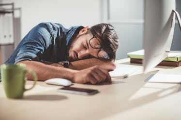 A man asleep at his desk with his laptop open.