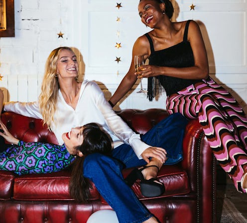 Three female friends enjoying a party and drinks huddled together on a couch in a small apartment